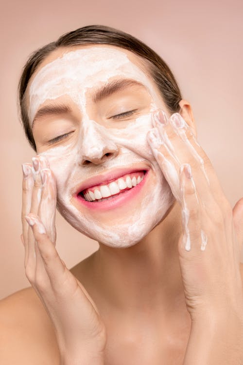 Free Smiling woman applies facial wash while enjoying her skincare routine, promoting happiness and skin health. Stock Photo